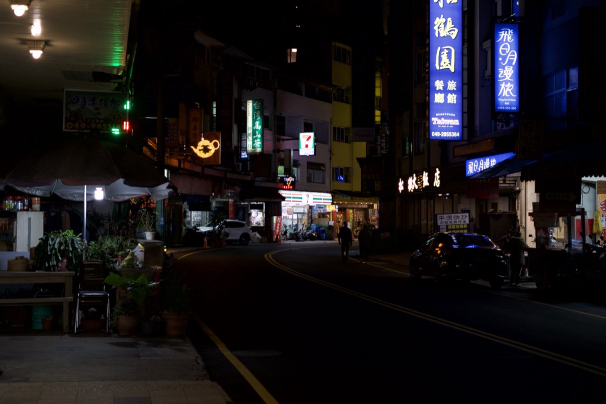 The same street exposed a stop darker, the neon signs holding their colour